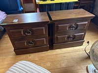 Pair of wood veneer nightstands with two drawers each, metal ring pull handles, sitting side by side on a hardwood floor with visible scratches on the tops.