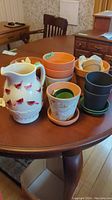 Photo showing the ceramic cardinal pitcher and various plant pots arranged on a wooden table