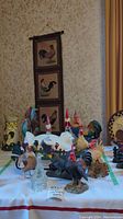 Wide view of table with multiple rooster-themed figurines and rooster fabric wall hanging behind