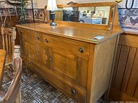Full view of the wooden sideboard buffet with three drawers, two cabinet doors, and a mirror back.