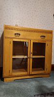 Front view of vintage wooden sideboard showing gold-tone drawer pulls, glass doors, and ornate trim