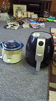 Photo showing Rival Crock-Pot slow cooker next to Ultrean air fryer on carpeted floor with other household items in the background.