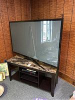 Samsung plasma display TV on wooden media stand with stone-look top, showing full items in lot.
