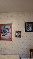 Wall with three hockey prints and photos: large color action print of Toronto Maple Leafs players, smaller central framed photo with gold frame, and a framed signed player photo with blue mat.