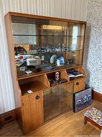 Wood-framed wall unit with three glass shelves, sliding glass doors on upper section, and wooden lower cabinet with two doors and open cubby holes.