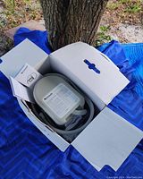 Ossur ice machine inside open box with power adapters and manual on blue blanket outdoors near a tree.