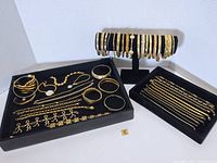Overall display of multiple gold tone bracelets on trays and a horizontal display stand.