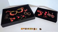 Two black velvet trays each holding a selection of red-themed costume pierced earrings, arranged neatly showing variety.