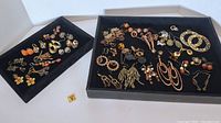 Overview of lot showing two black trays filled with assorted pairs of pierced costume earrings with orange and gold tones prominently visible.