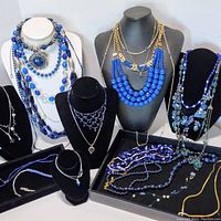 Overview photo showing the full collection of blue costume necklaces on black and white stands and trays.