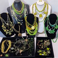 Front view showing multiple green fashion/costume necklaces displayed on black and white busts, with trays of bracelets and necklaces below.