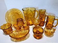 Full lot of thirteen amber glass pieces showing variety of items and patterns.