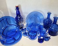 Photo showing the entire collection of vintage blue and cobalt glass pieces including serving trays, bottles, goblets, bowl, and candle holders