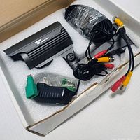 Top view of Night Owl camera with cables and power supply in box foam packaging.