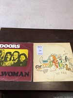 Both vinyl LP album covers: The Doors L.A. Woman on left and Crosby, Stills Nash and Young So Far on right placed on dark surface.
