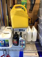 Yellow 20 liter diesel gas tank with multiple plastic containers including Valvoline DEF and various diesel fuel additive bottles on a metal shelf.