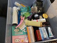 Clear plastic bin with assorted beauty products, hair clips, face masks, and cosmetic bottles