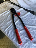 Full view of the Milwaukee bolt cutter on a white textured surface showing the red grips and black cutting jaws.