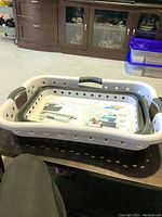 Full view of the gray and white plastic laundry basket on a table with visible ventilation holes and grip handles.