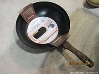 Top view of the wok pan showing black interior and wooden handle with attached labels.