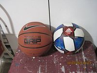 Photo showing Nike basketball on the left and Adidas soccer ball on the right, placed on a paint-splattered surface against a white background.