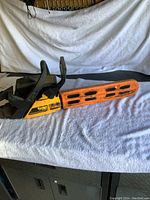 Side view of Poulan 255 Pro chainsaw with orange protective bar cover on a white towel backdrop.