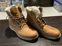 Front angle view of both boots showing tan leather, fur lining, lace-up detail and soles.