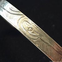 Close-up photo showing one side of the silver bangle with abstract and geometric engravings including cross-hatching textures.