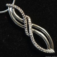 Close-up front view of the twisted loop sterling silver pendant with embedded clear stones on black background.