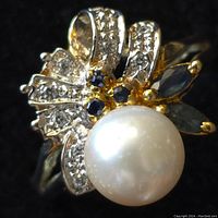 Close up of silver ring with freshwater pearl and blue and clear stones, showing detailed floral design and pearl luster.