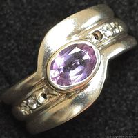 Close up of sterling silver ring with oval purple gemstone and two small clear accent stones on black background