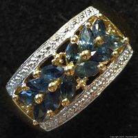 Close-up front view of silver ring with rectangular frame, clear stones on edges, and nine marquise-shaped blue sapphire stones inside.