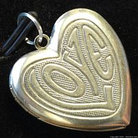 Front view of heart-shaped silver locket pendant showing raised 'LOVE' engraving.