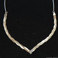 Close-up of the sterling silver necklace showing the twisted textured V-shaped centerpiece on a thin wire chain against a black background.