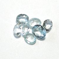 Seven clear, light blue oval faceted aquamarine gemstones spread out on white background.