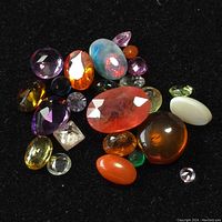 Image showing a variety of loose faceted and cabochon assorted gemstones in multiple colors and shapes on a black velvet surface.