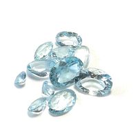 Top view of ten light blue transparent faceted blue topaz gemstones in oval and teardrop shapes on white background.