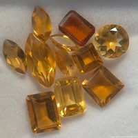 Loose citrine gemstones in various shapes and hues laid out on a soft surface, showing color and cut details.
