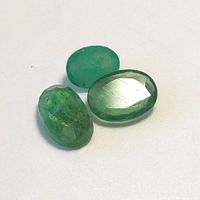 Three green oval emerald gemstones with polished surfaces shown from above on a white background