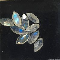 Ten marquise-cut moonstone gemstones displayed on black background, showing blue adularescence and faceted surfaces.