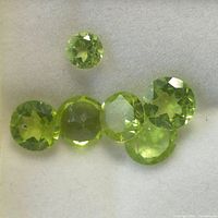 Six round faceted peridot gemstones displayed on white background