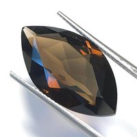 Faceted marquise cut smokey quartz gemstone held by tweezers showing its color and facets.