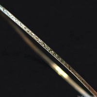 Close-up photo highlighting the engraved pattern on the slender silver bangle bracelet, showing intricate detailing and polish.