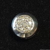 Close-up of round sterling silver diamond cluster pendant on black background.