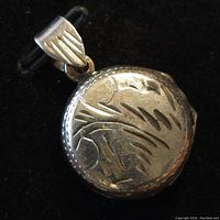 Front side of the round sterling silver locket pendant showing engraved floral and leaf patterns and textured edge.