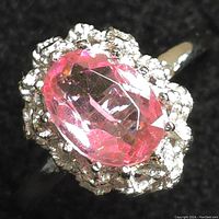 Close-up photo showing the pink oval faceted gemstone with clear stones surrounding it on a sterling silver ring band.