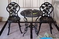 Front view of two black cast metal rose design bistro chairs paired with round table.