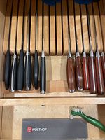 Chef knives with varying handle materials in wooden knife organizer drawer.