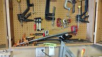 Wide shot of pegboard shelf showing assortment of bar clamps and smaller clamps