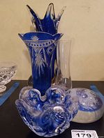 View of the lot with the large cut-to-clear vase, smaller clear vase, blue and clear bowl, paperweight, and floral etched bowl visible on the table.